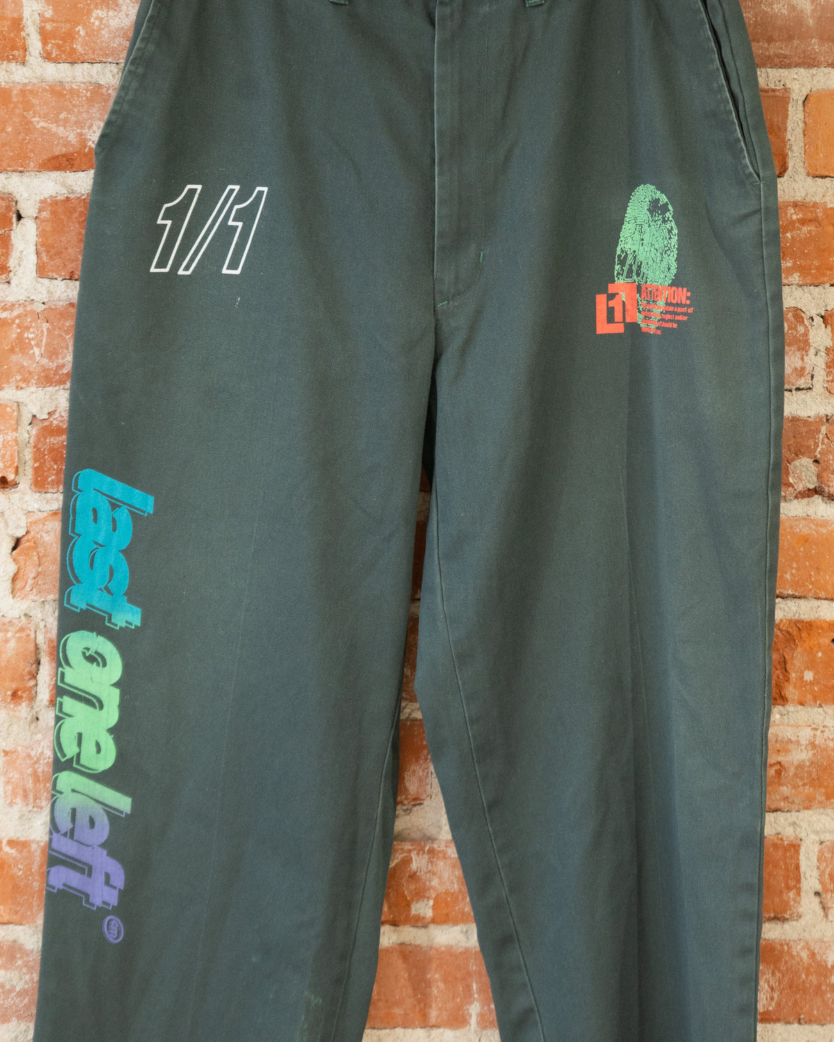 Closeup of green vintage pants with multicolored screenprinted designs on them.
