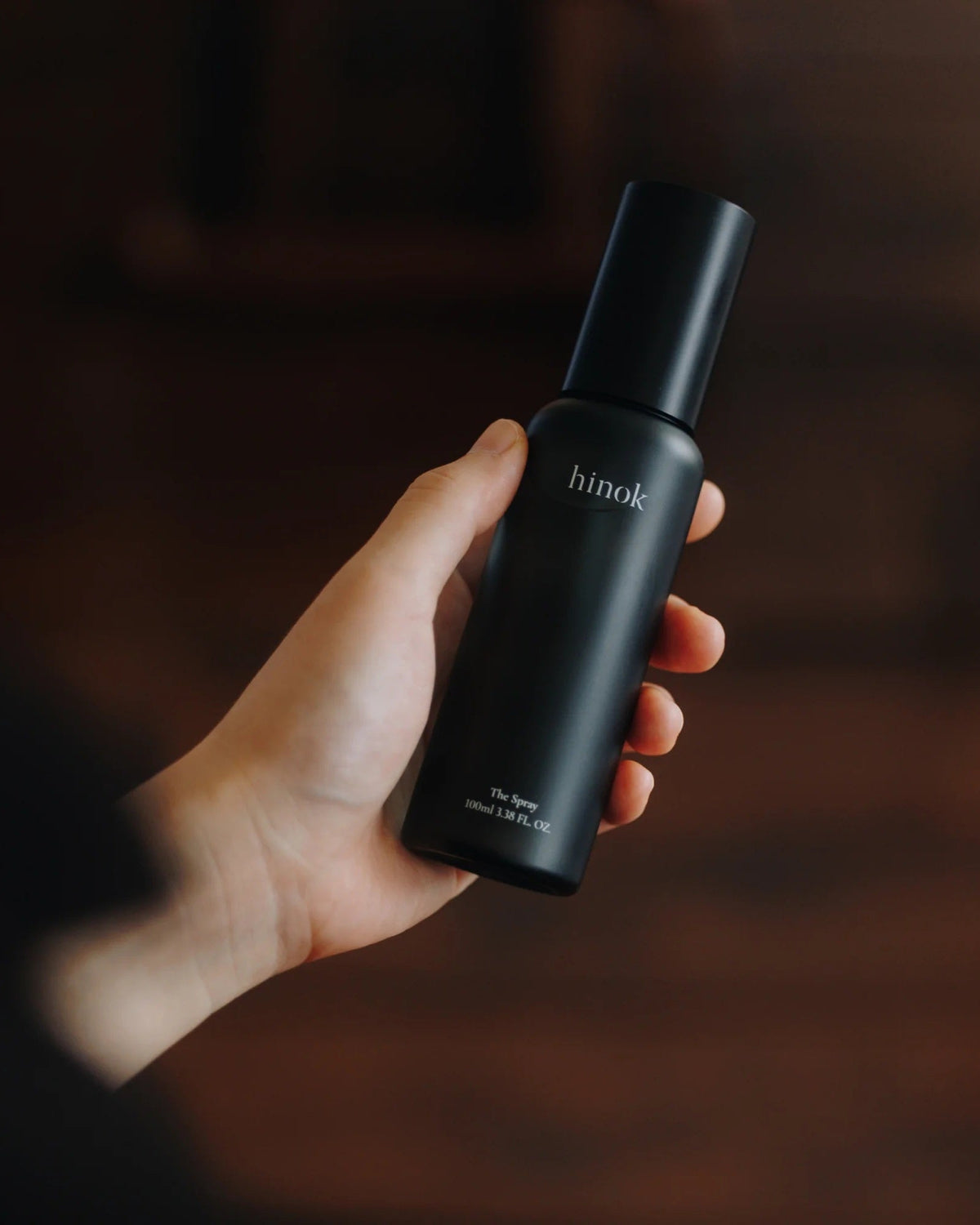 A person's hand holding hinok The Spray in travel size.
