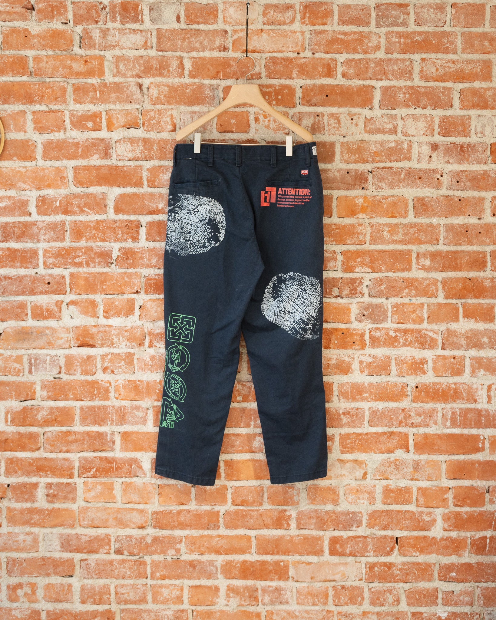 Navy vintage pants with white, green, and orange screenprinted designs on them.