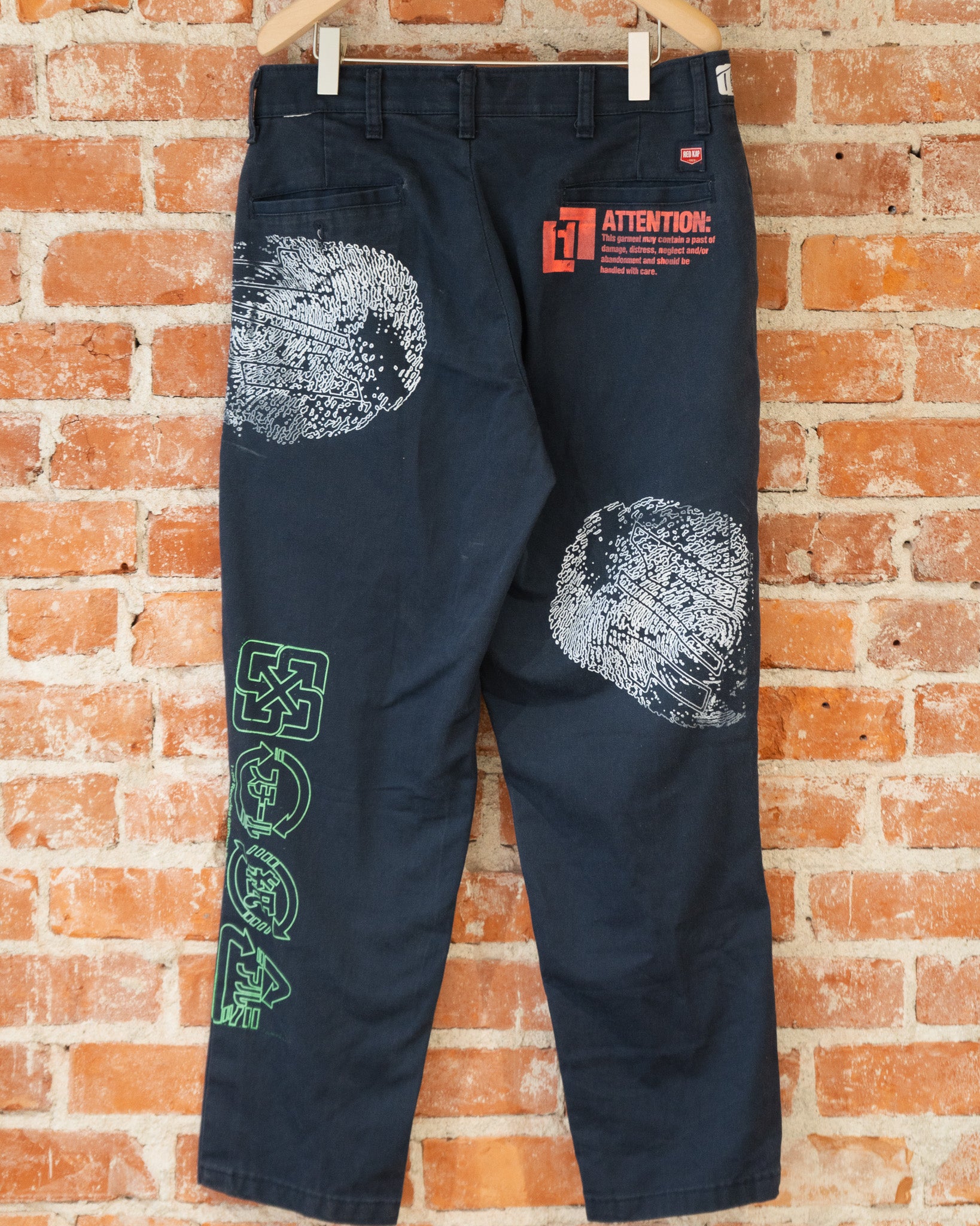 Navy vintage pants with white, green, and orange screenprinted designs on them.