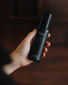 A person's hand holding hinok The Spray in travel size.