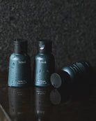Three travel-sized bottles of different hinok hair and body formulas, covered with beads of water.